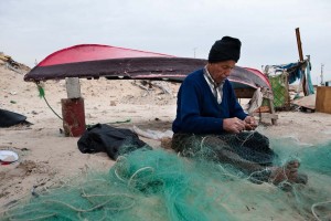 Using time-honored techniques, an elderly Palestinian fisherman mends his nets on the beach at Gaza City. Gaza's once large and prosperous commercial fishing fleet now lies crippled by lack of spare parts due to the Israeli blockade on most imports.
