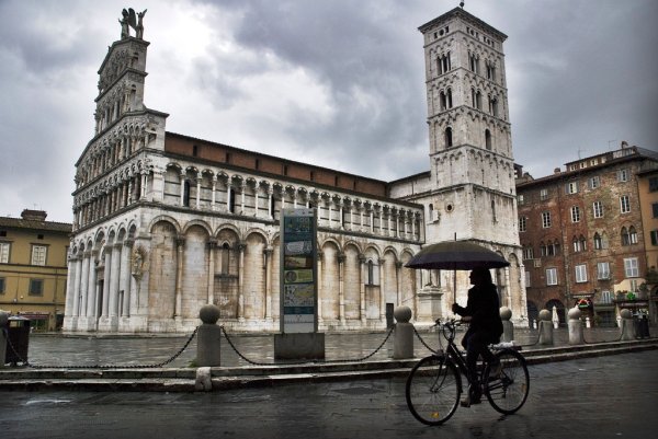Woman cycling with umbrella in Lucca, Italy
