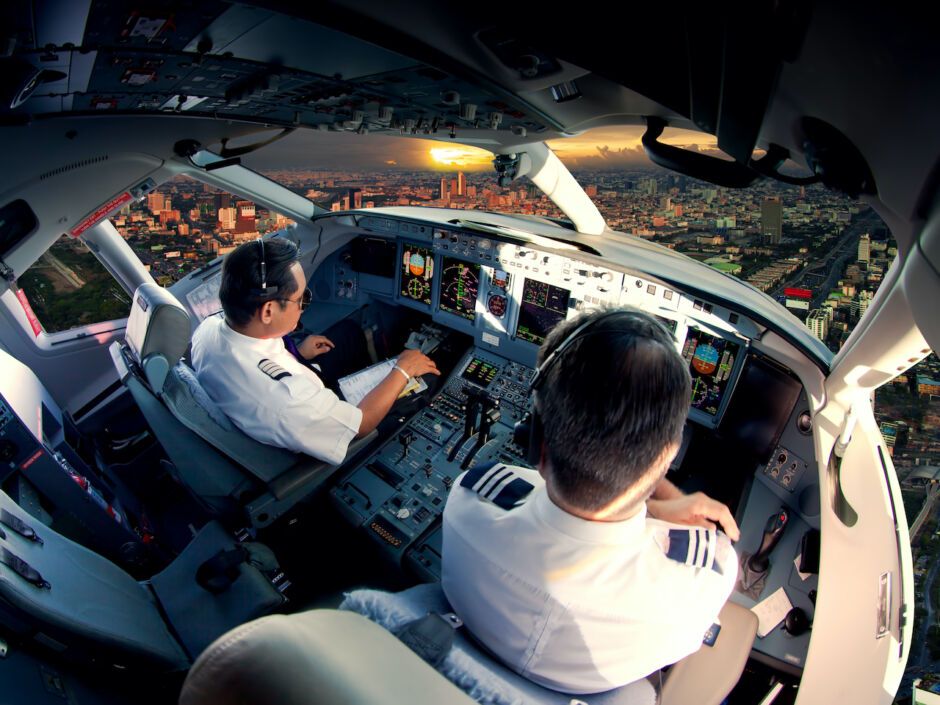 Two pilots in a commercial aircraft cockpit with cityscape at sunset