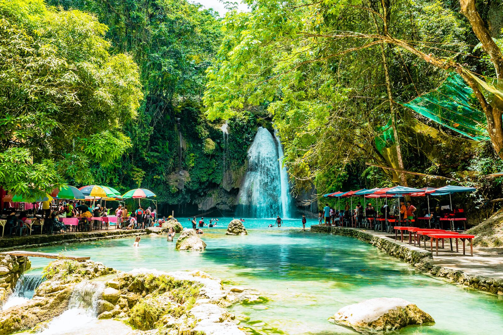 Mulit colored umbrellas and red benches at Kawasan Falls, where people are eating and swimming