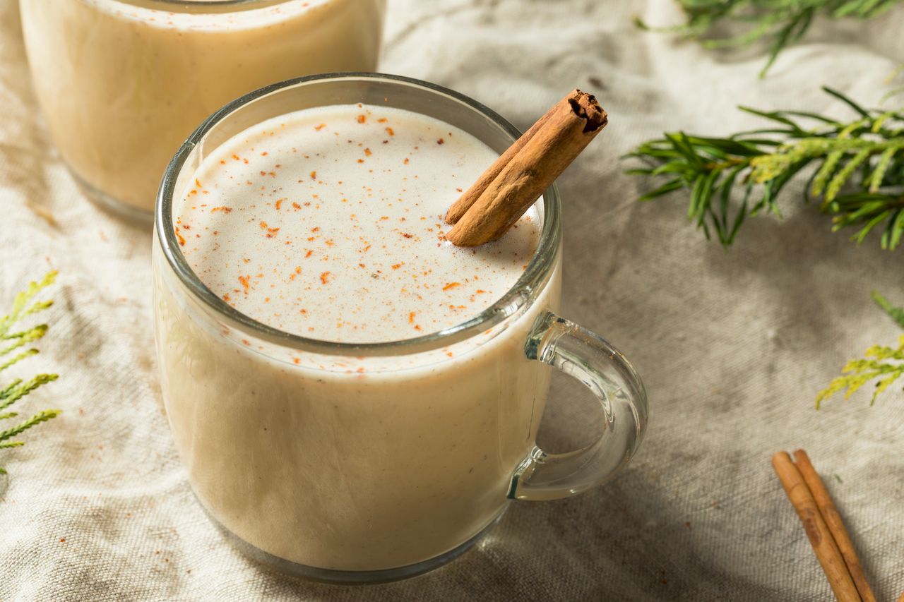 glass of coquito with a cinnamon stick against a white background