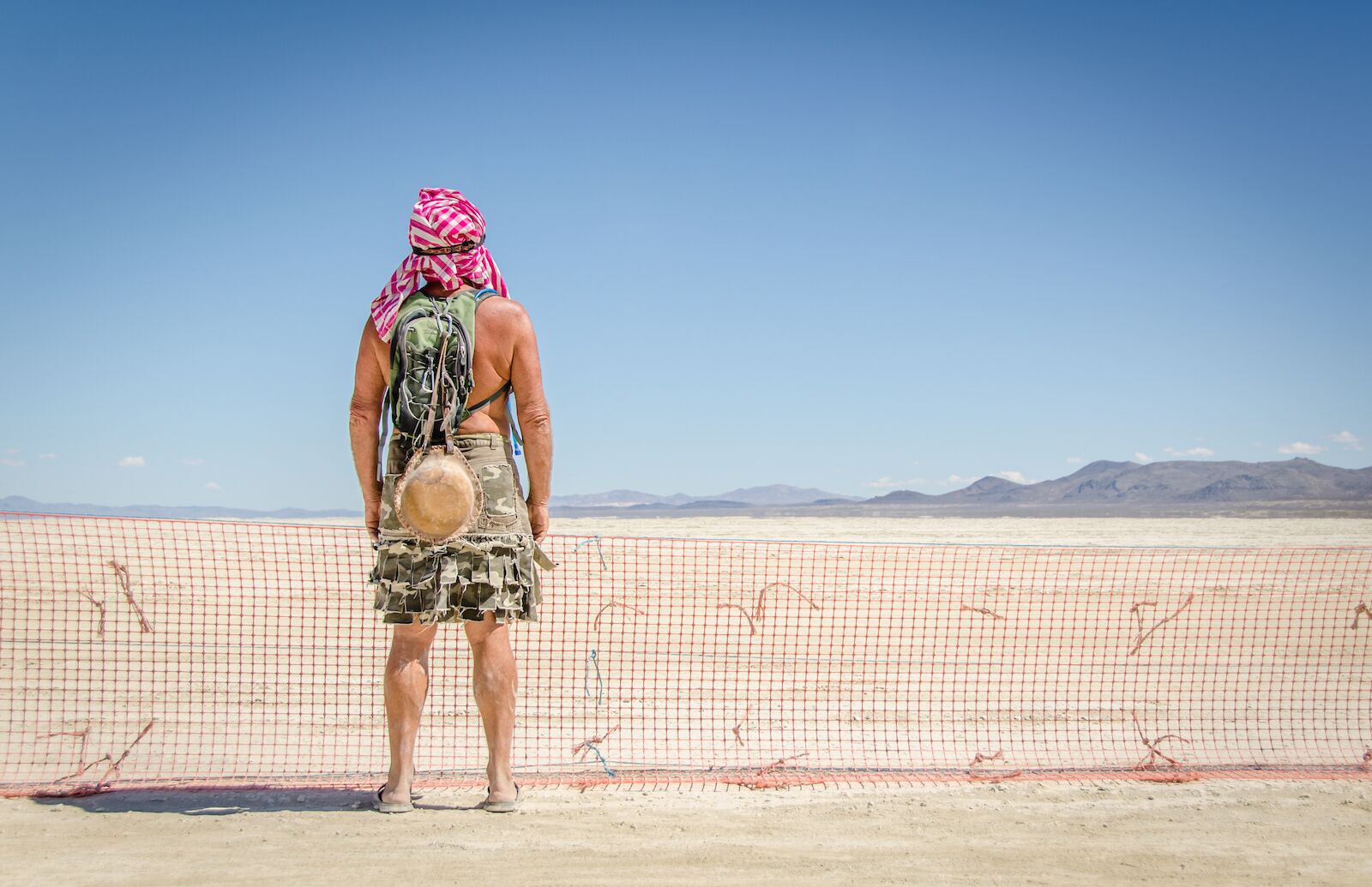 man against a fence at burning man with gear