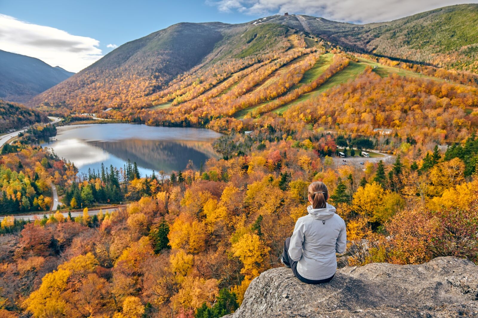 Woman hiking at Artist's Bluff in autumn. View of Echo Lake. Fall colours in Franconia Notch State Park. White Mountain National Forest, New Hampshire