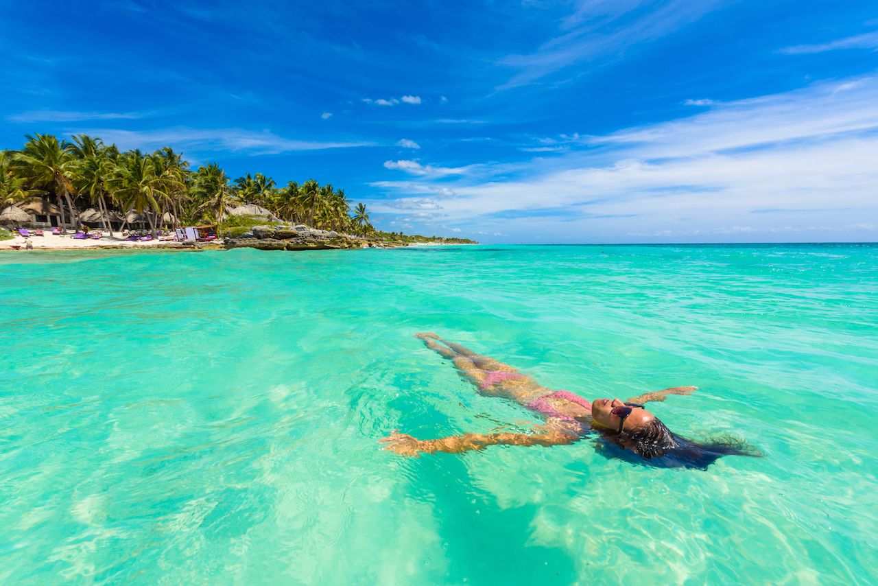 Young woman relaxing in turquoise waters of Caribbean Sea in front of paradise beach in Tulum, close to Cancun, Riviera Maya, Mexico