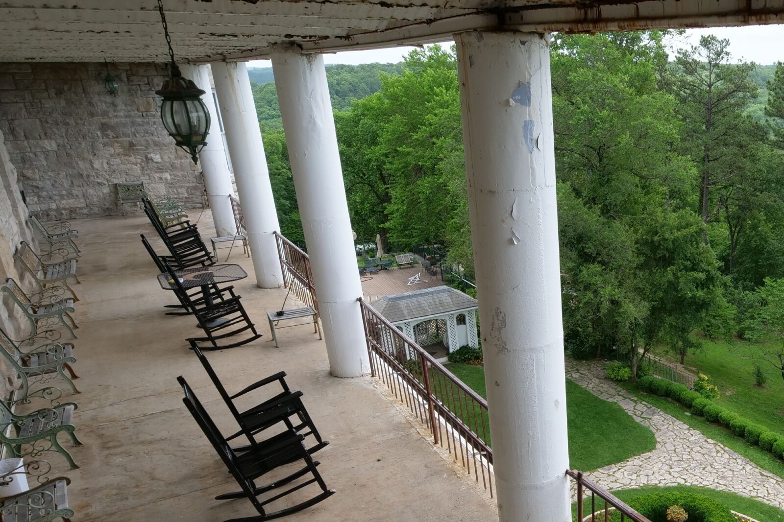 Back porch of the Crescent Hotel and Spa with wicker chairs, rocking chairs and peeling paint on the roofs and pillars overlooking a garden