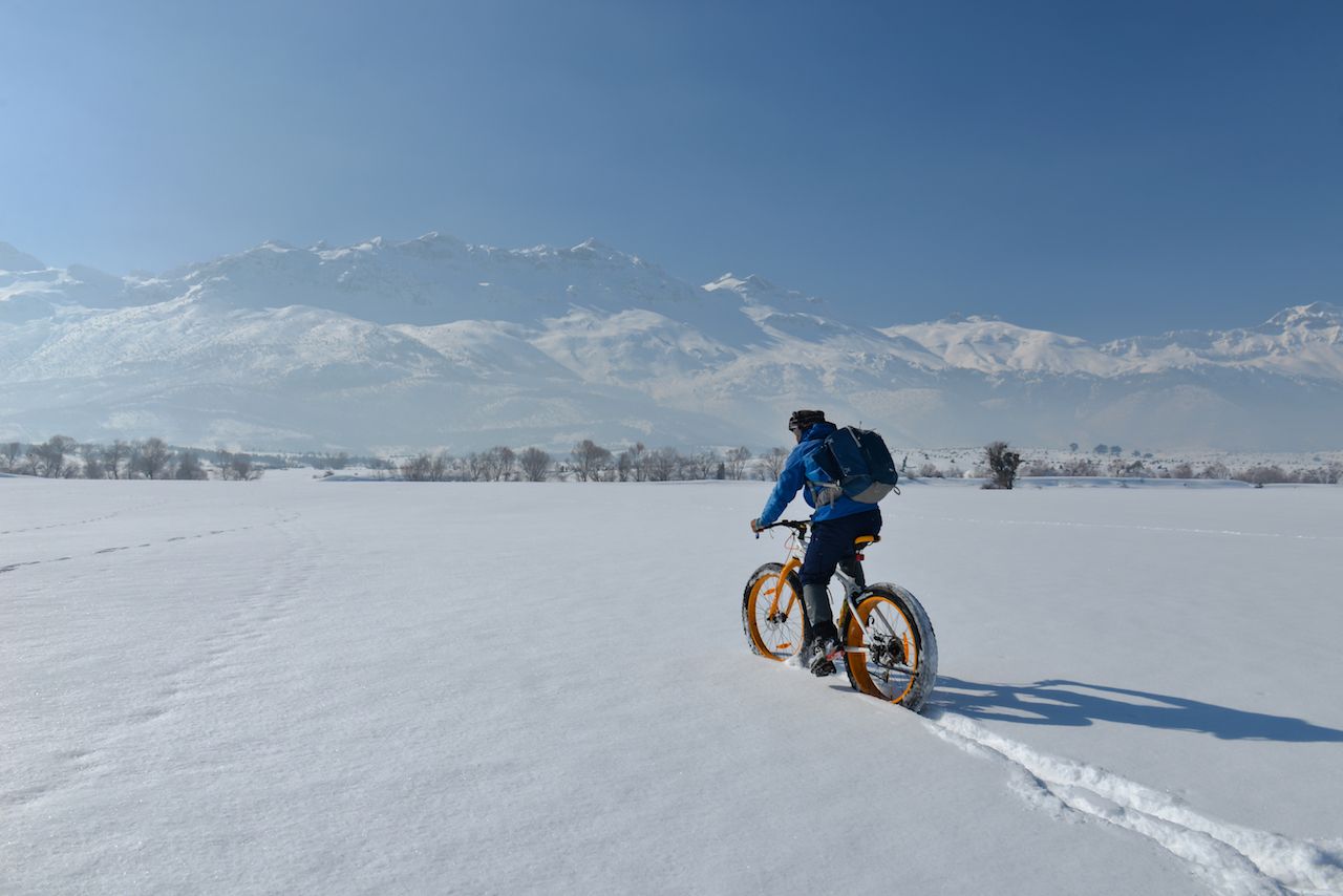Person fat biking through the snow, with mountains in the background
