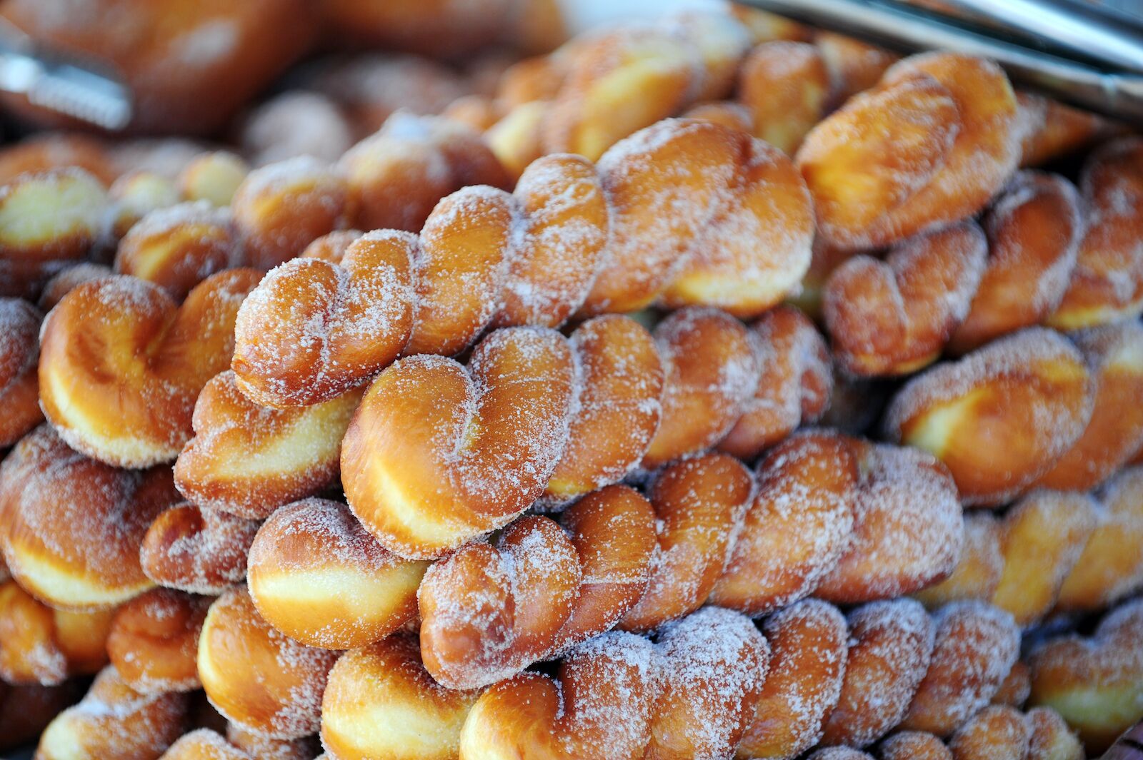 A stack of twiested donuts sprinkled with sugar at a bakery