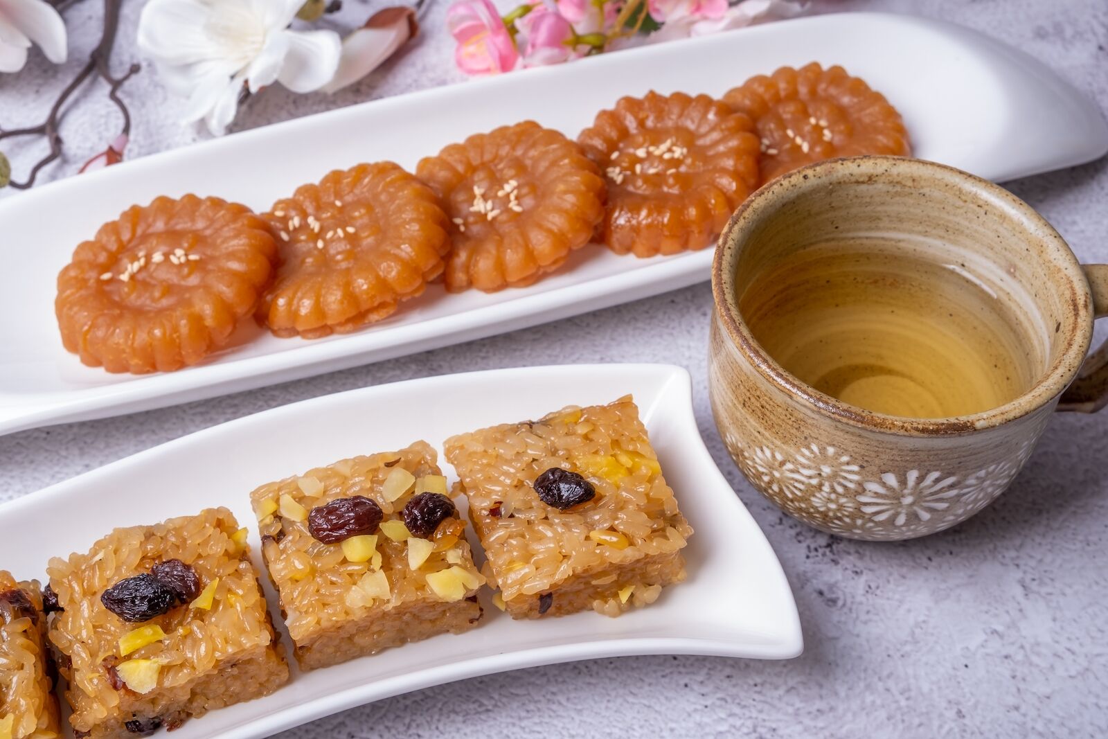 a long thin rectangular plate of yaksik, or sticky rice cakes, with red dates, next to a cup of tea and plate of honey cookies