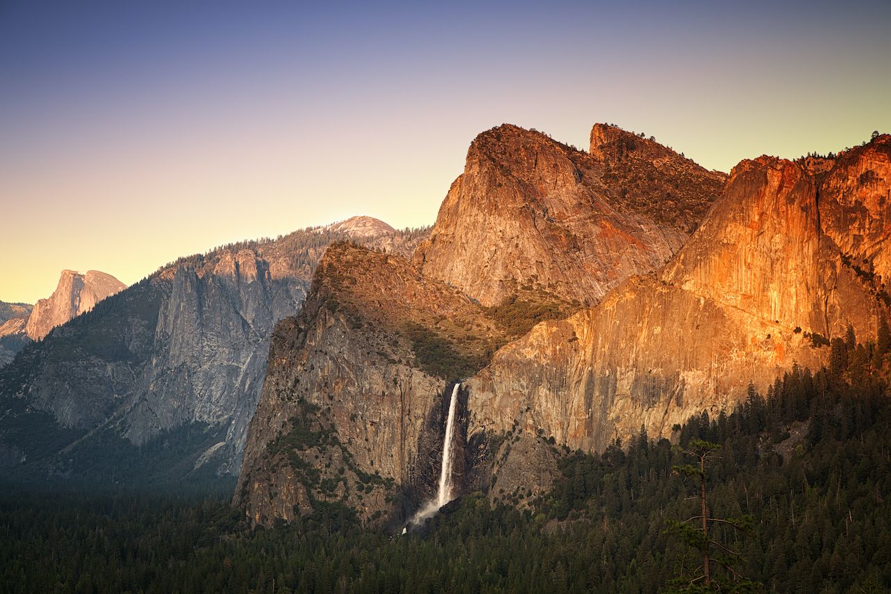 Yosemite at sunset as seen from the Tunnel View viewing point, showing the Half Dome, Cathedral Rocks and the Bridalveil Falls being lit by the setting sun. Yosemite National Park, California, USA