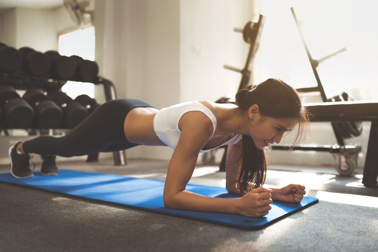 Woman holds a plank pose on a mat in a gym