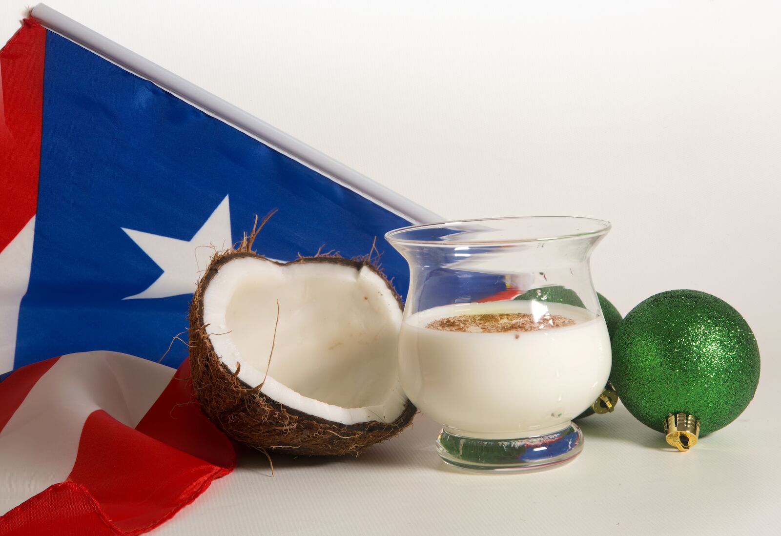 a glass of coquito next to a coconut with the puerto rican flag in the background