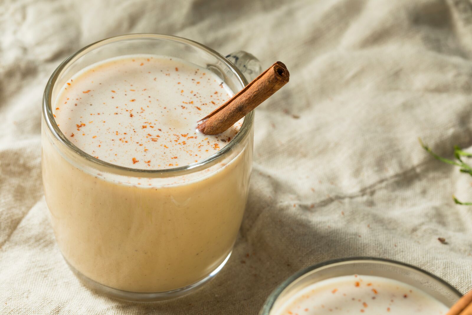 a glass of coquito with a cinnamon stick sprinkled with cinnamon