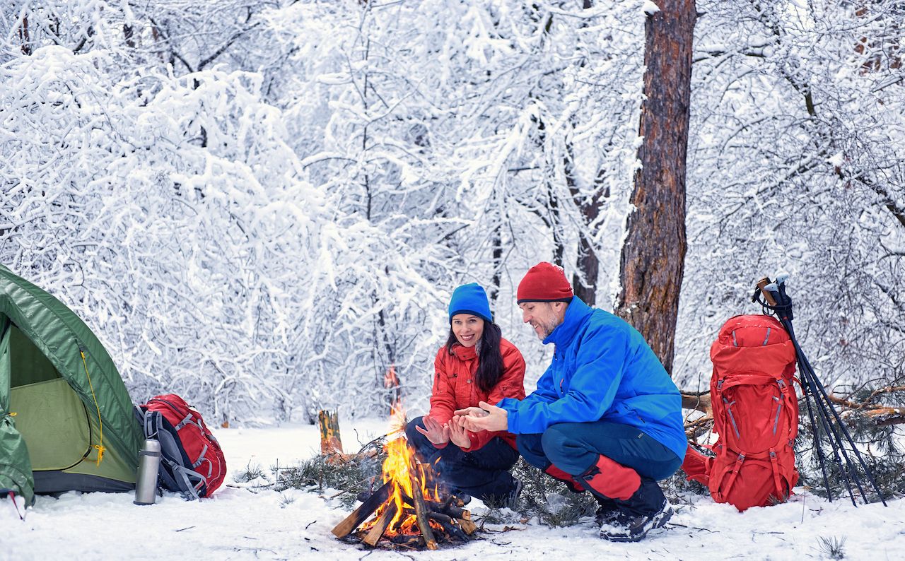 A couple huddles over a campfire at a snowy campsite