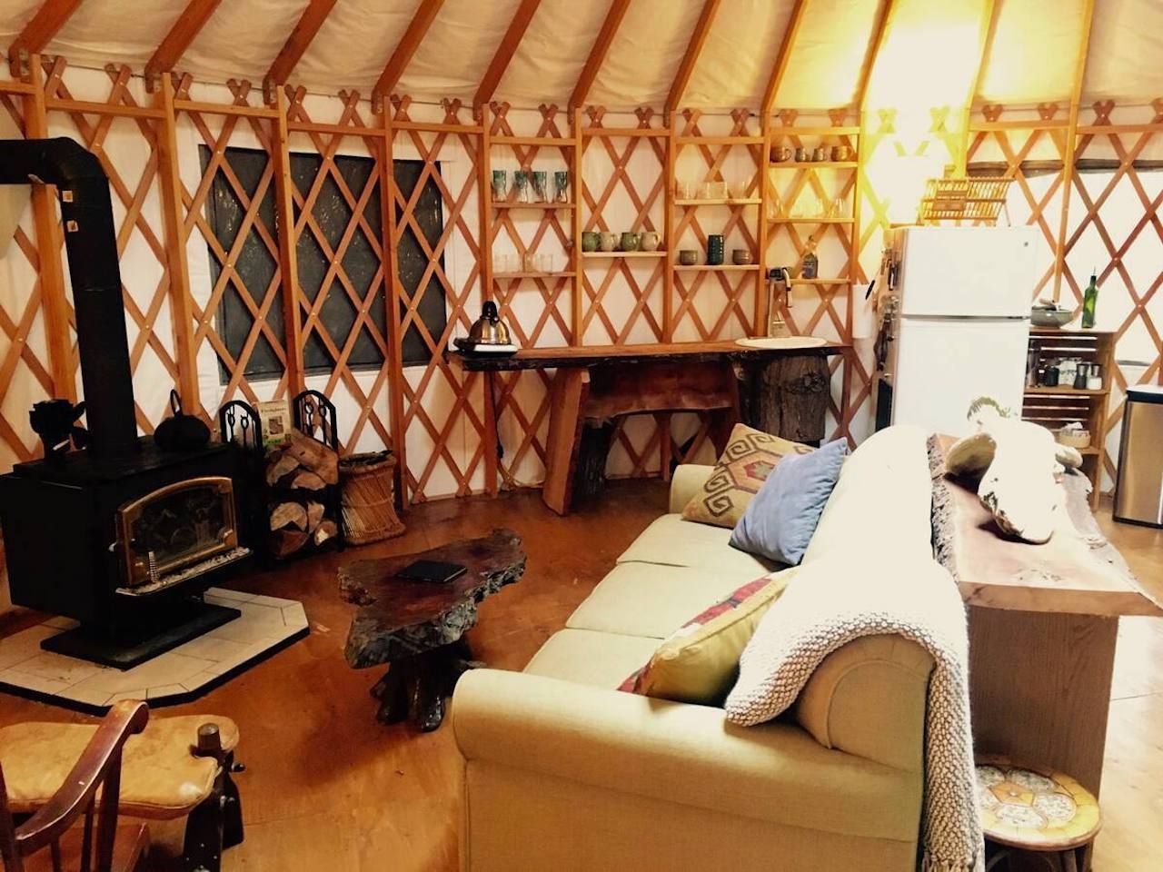 The cozy interior of a modern yurt with a couch, fridge, and wood stove