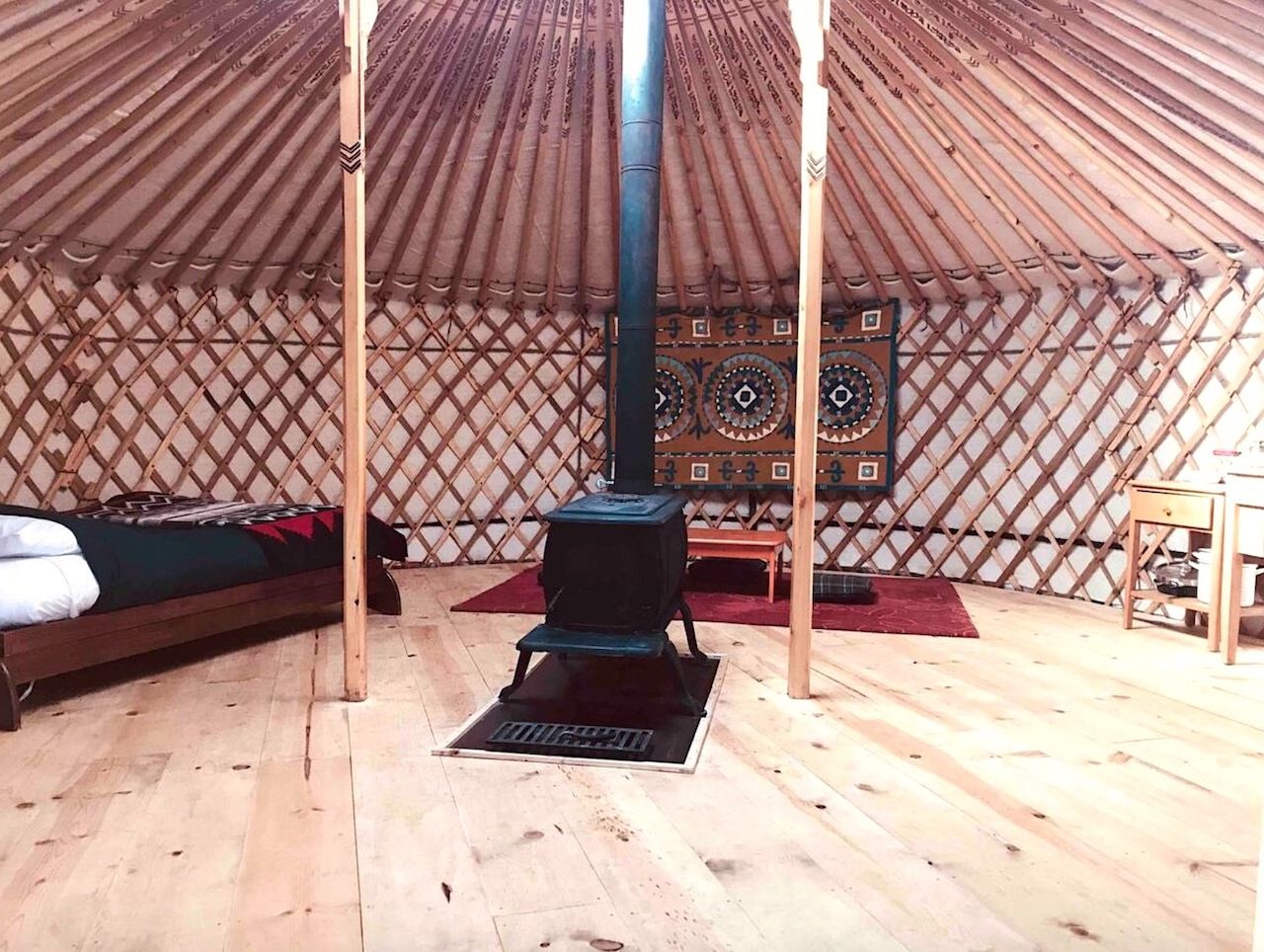 The uncluttered interior of a modern yurt with a wood stove and double bed