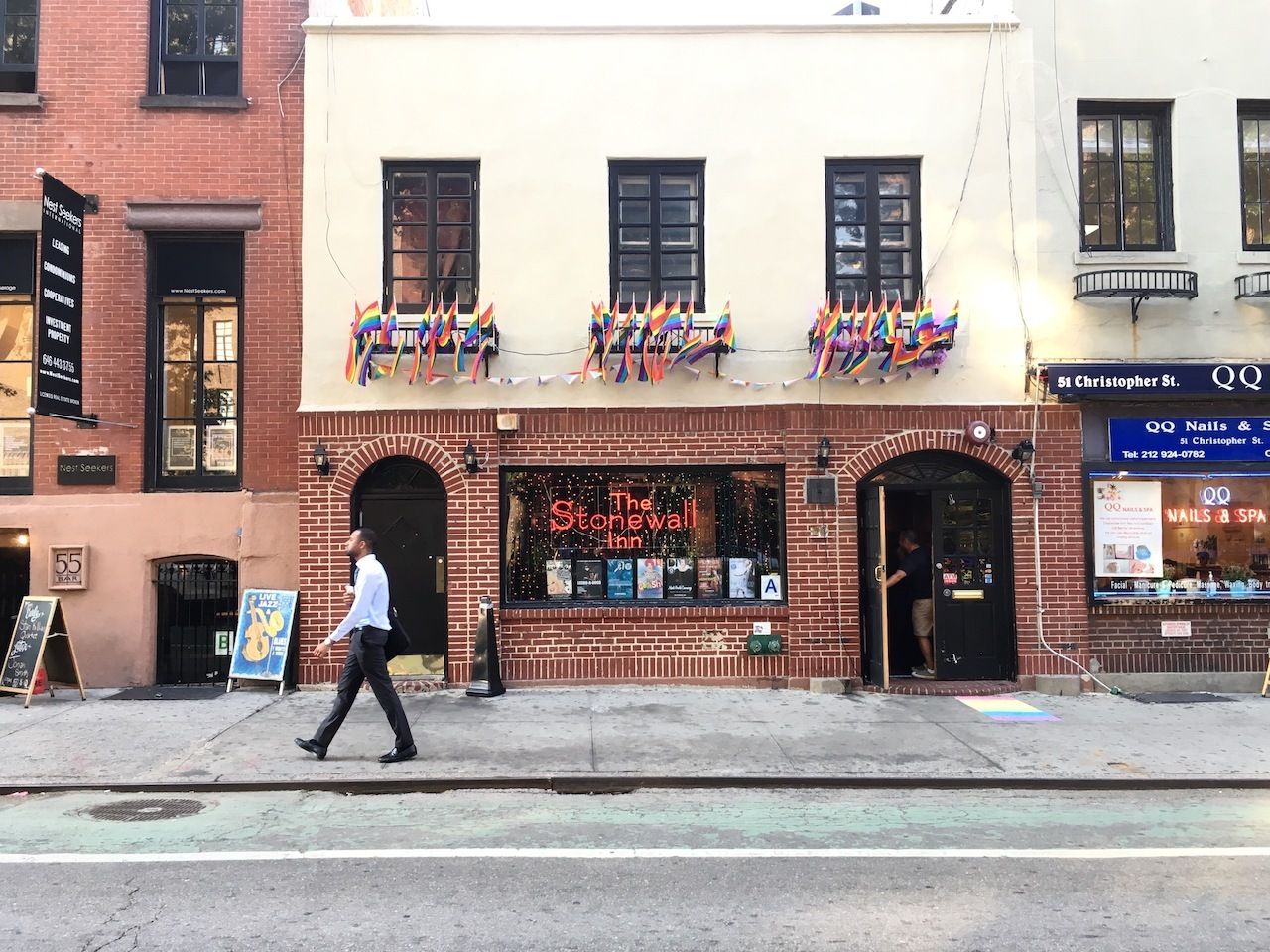 NEW YORK CITY - 12 JULY 2016: A businessman walks in front of the Stonewall Inn on Christopher Street, the location of the Stonewall riots and the birth of the gay rights movement., LGBTQ safe spaces US