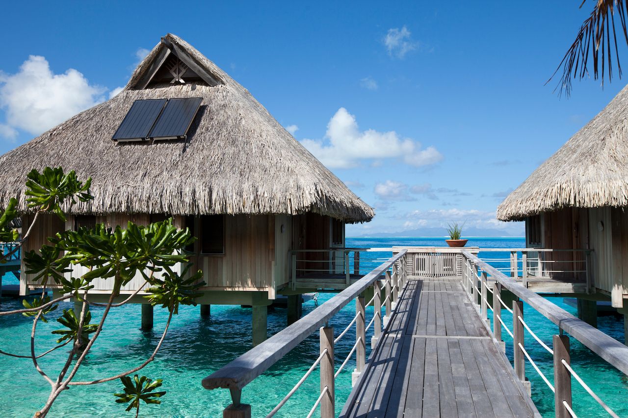 Wooden walkways over the water of the blue tropical sea to authentic traditional Polynesian thatched roof houses with eco-friendly use of solar panels. Polynesia, Tahiti