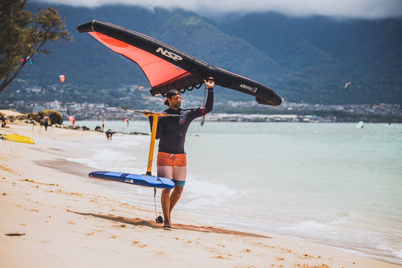 Pro wind foiler walking with kite and board on the beach