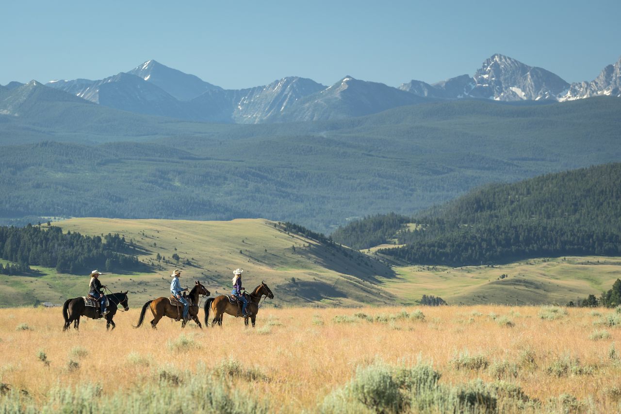 Three guests horseback riding at the Ranch at Rock Creek, with mountains in the background