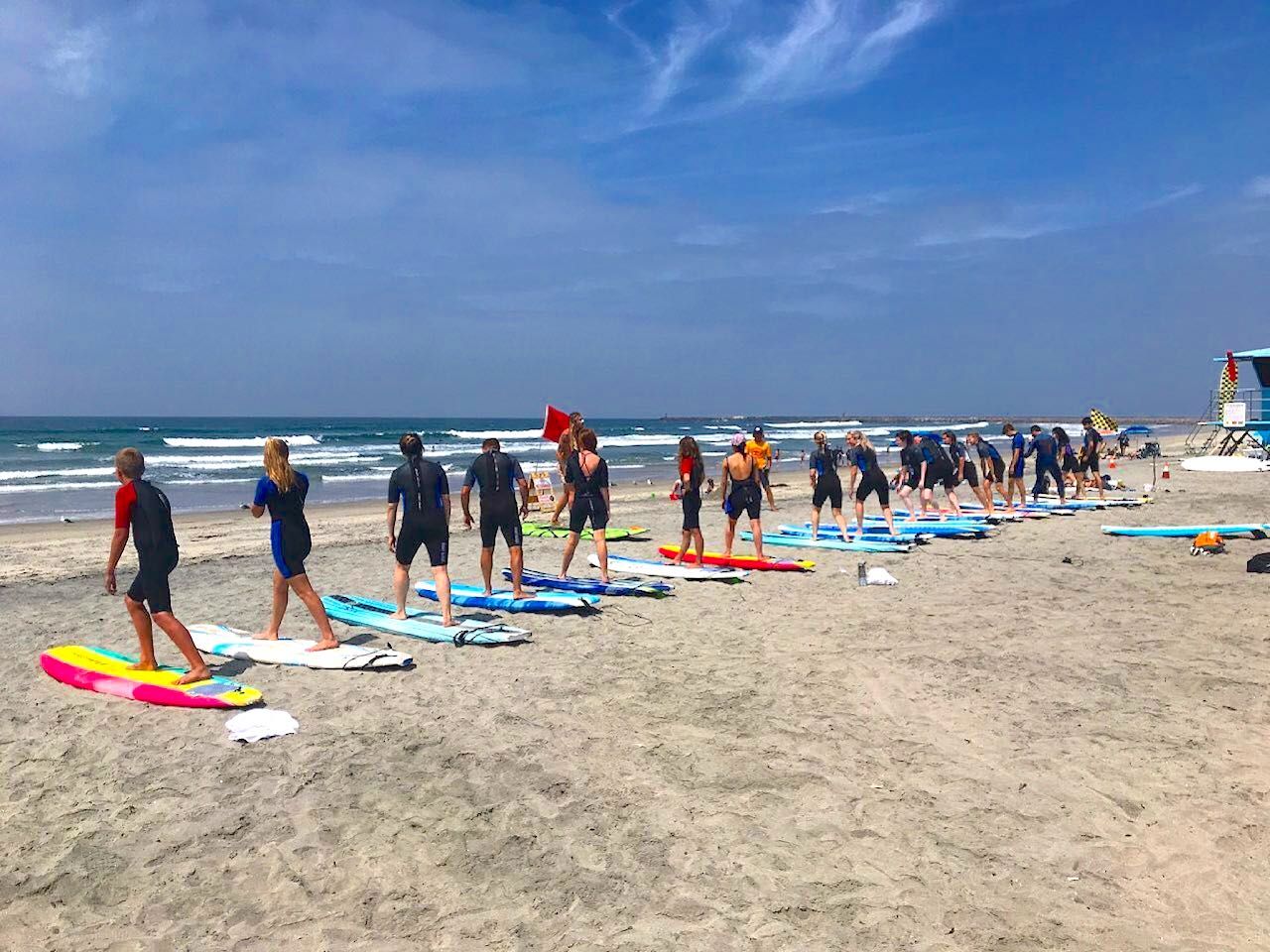 Learning surfers lined up on beach next to surfboards