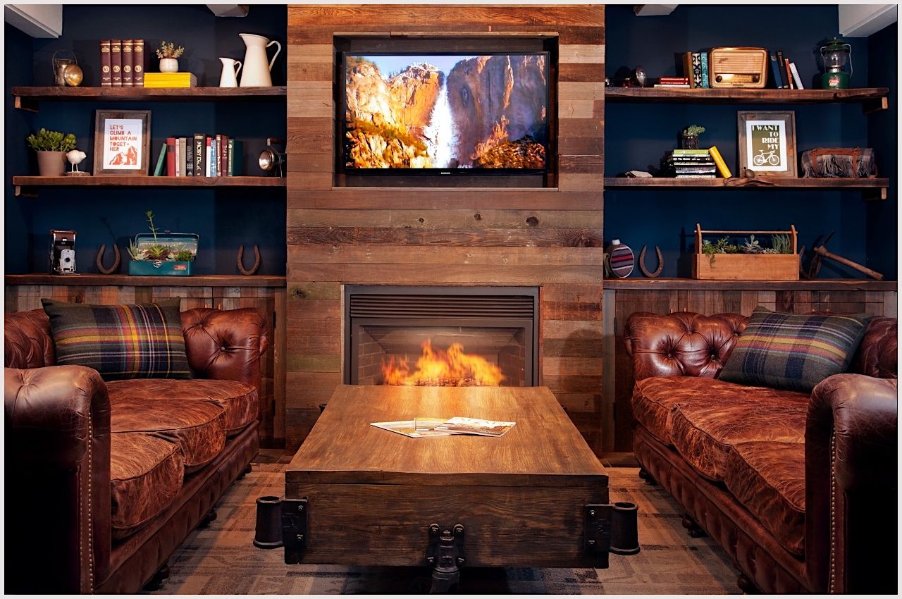 The cozy living room at Basecamp Tahoe South, a Lake Tahoe hotel, has leather couches, a fireplace, and bookshelves