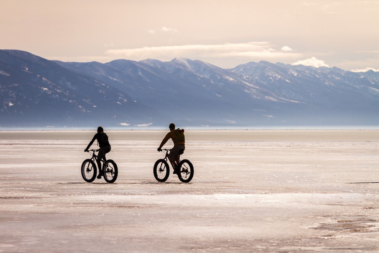 Two bicyclists ride fat tire bikes across a frozen Flathead lake
