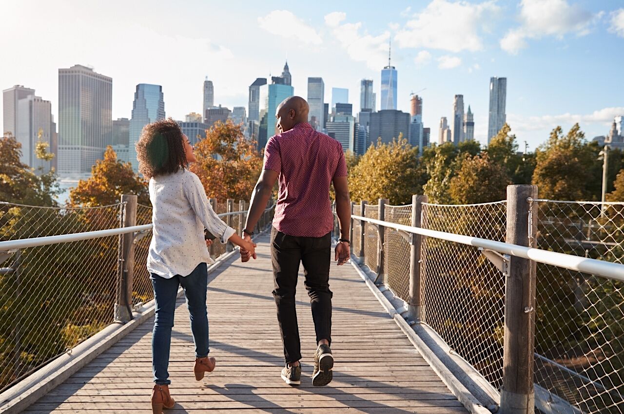 Couple walking on decked area with New York skyline in the background 