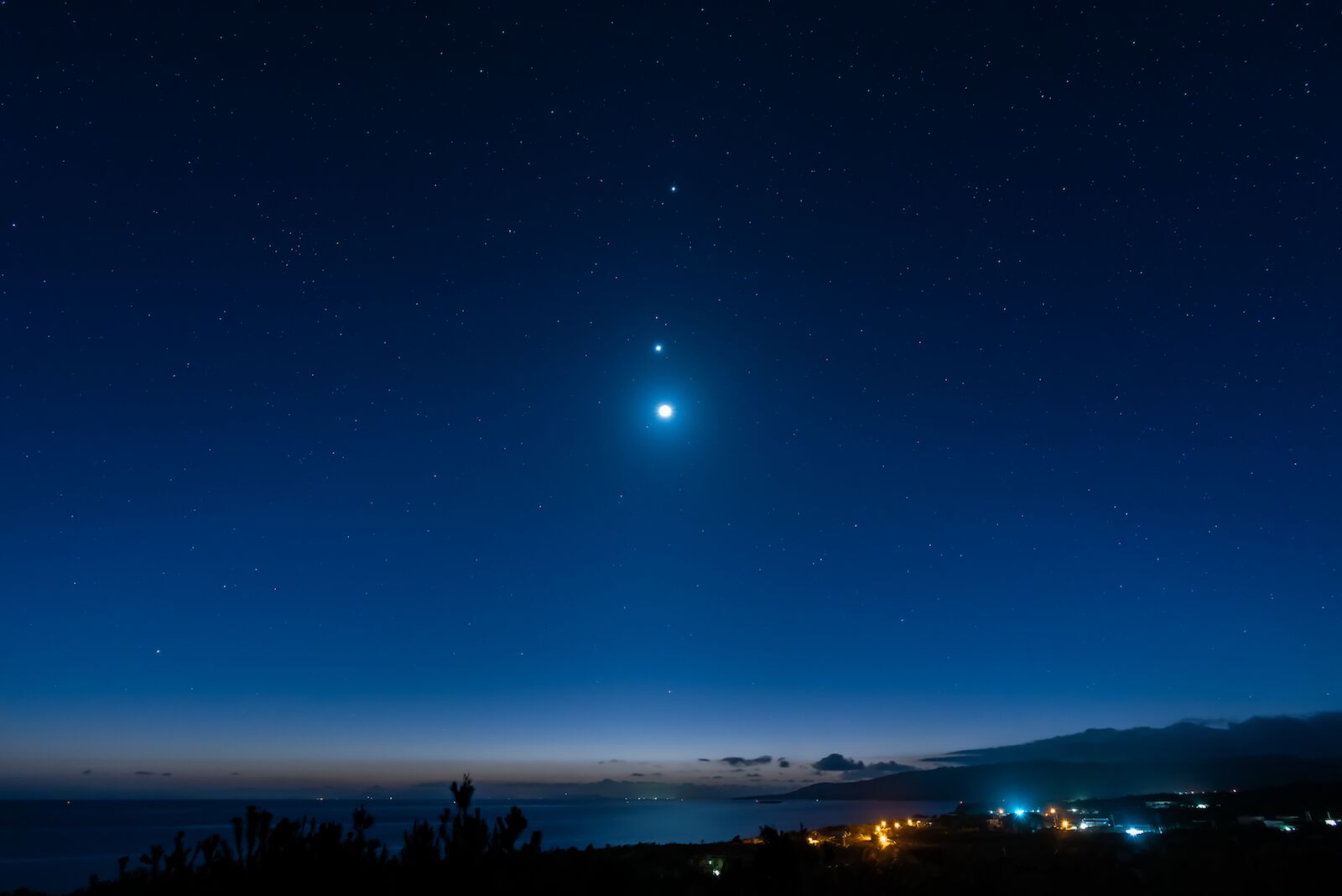 Breathtaking view of a starry sky, Venus, Jupiter and moon line up. Top view of a seashore city before dawn. Iriomote Island, natural world heritage.
