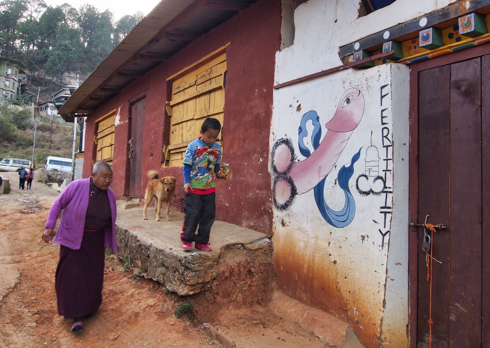 Child and grand mother walking by the painting of a penis in Bhutan
