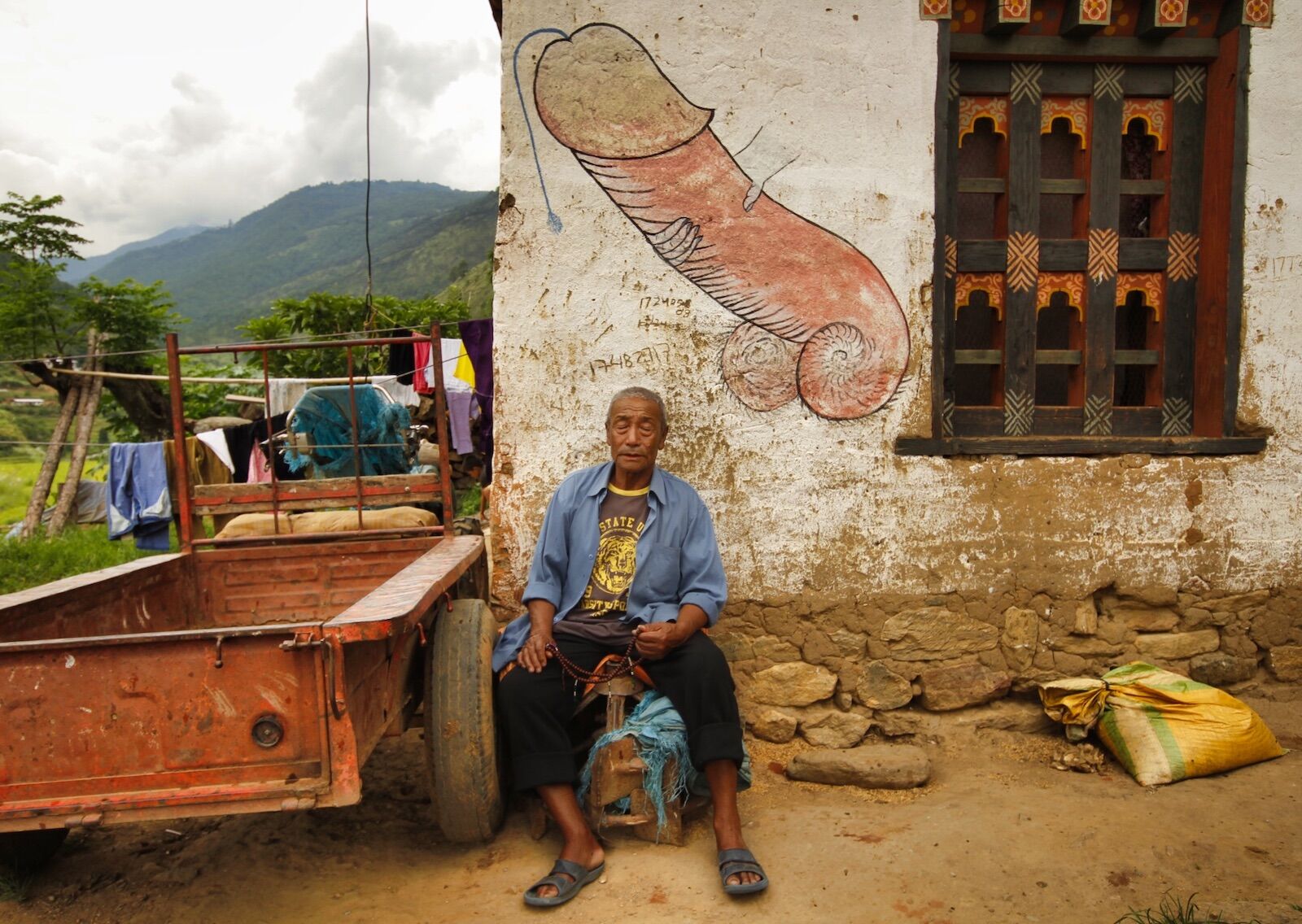 Man sitting under the painting of a penis in Bhutan