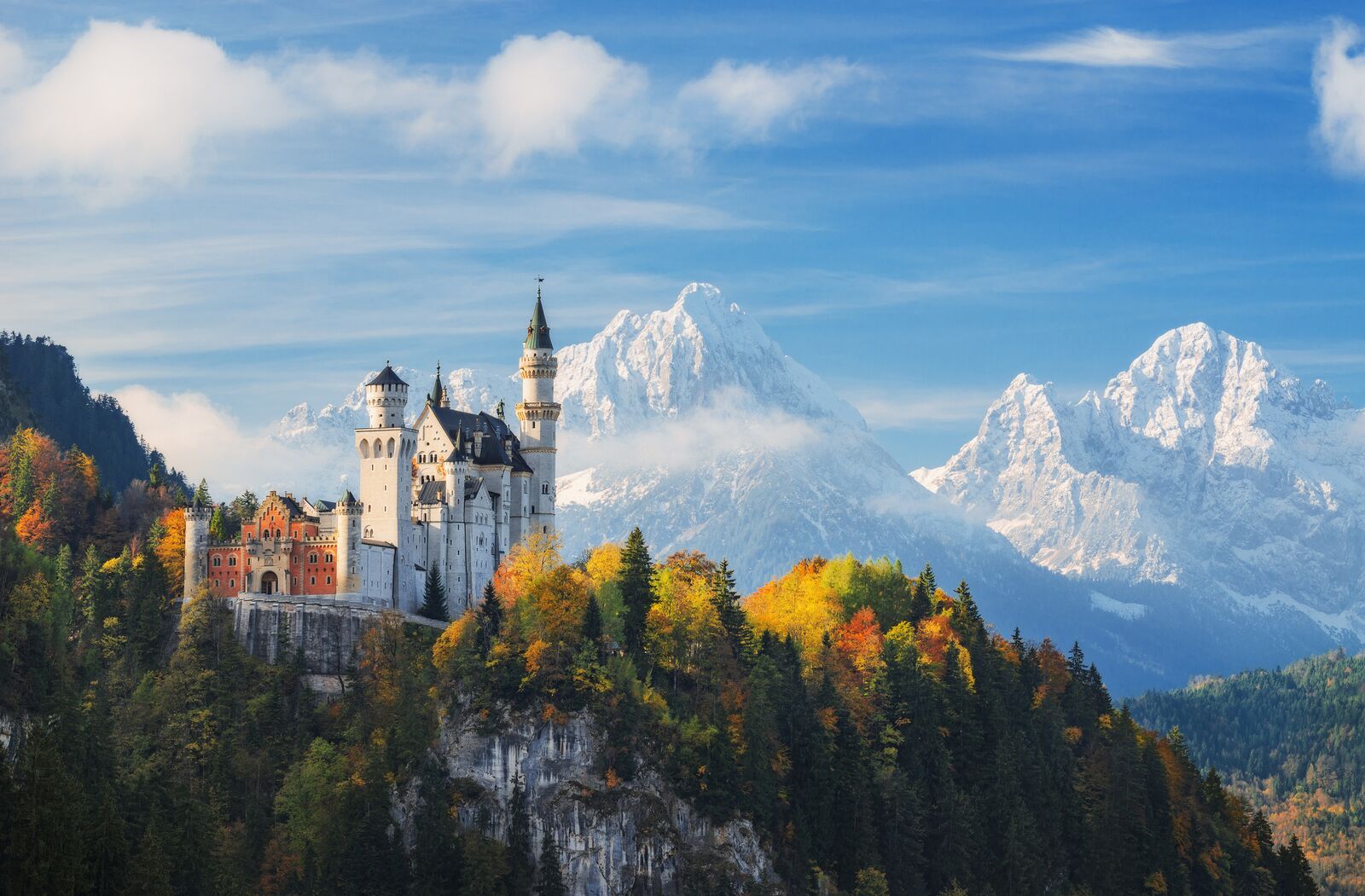 Germany. The famous Neuschwanstein Castle in the background of snowy mountains and trees with yellow and green leaves.