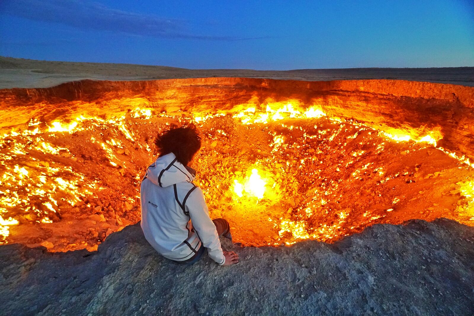 Man sitting on the edge of the "Gat to Hell" in Darvaza, Turkmenistan