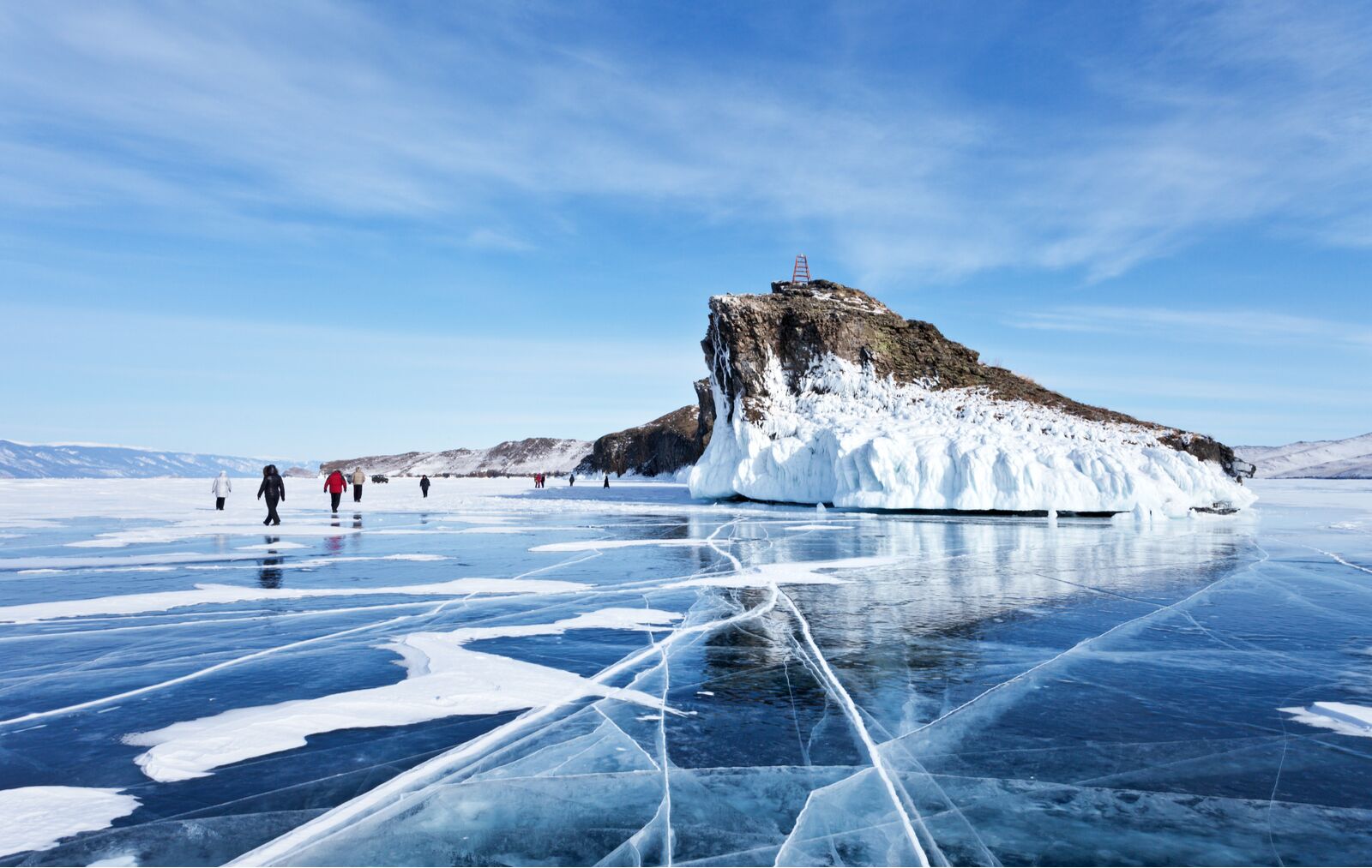 A group of tourists travels along the ice of the frozen Lake Baikal. Excursion to the beautiful iced rocks of Horin-Irgi or Cape Kobyliya Golova