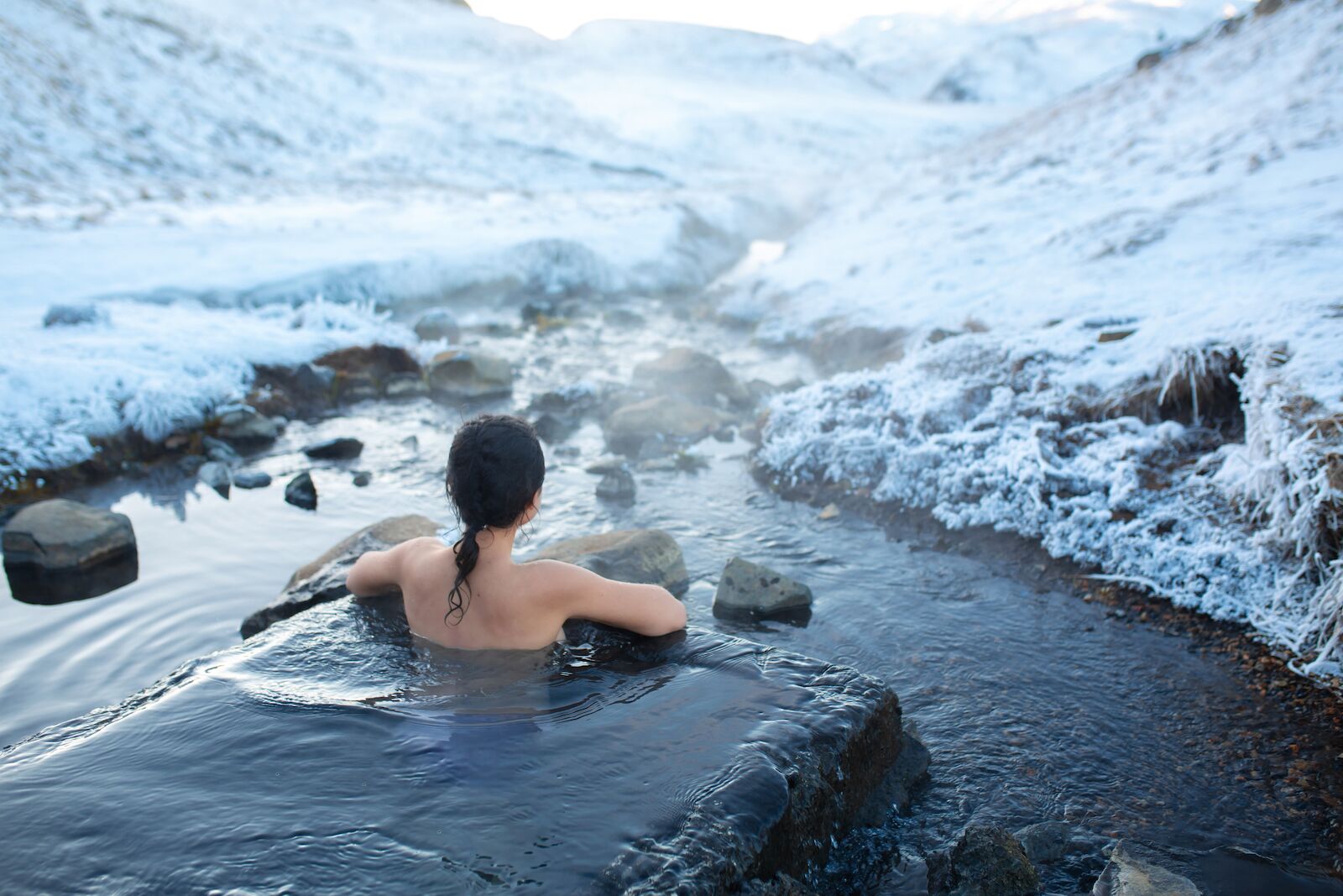 Person naked enjoying the warm waters of a hot spring in Iceland with views of snowy mountains. Iceland is a great destination for Spring Break 2022.