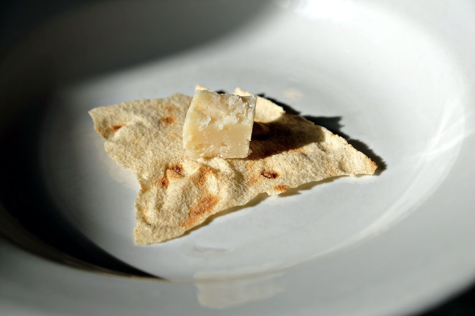 small cube of "Casu marzu", a typical sardinian cheese on a sheet of "Pane carasau", a thin crisp sardinian bread