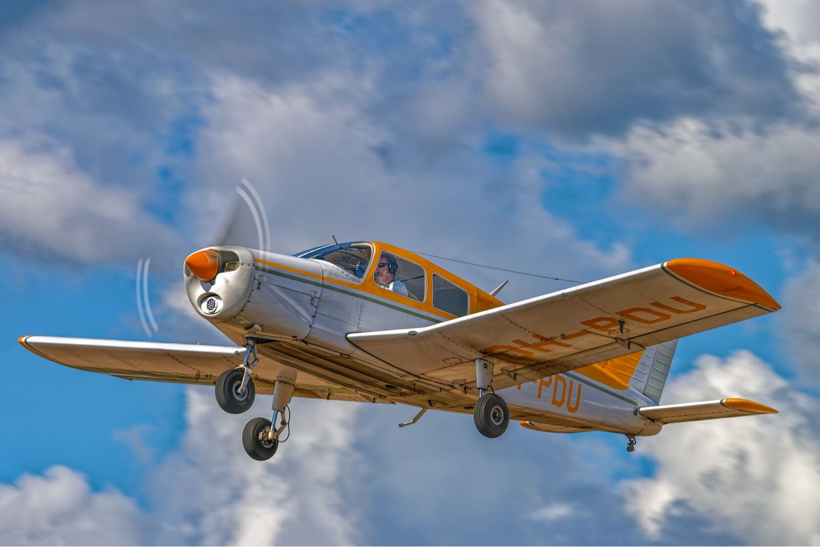 Four-seat light all-metal single-engined piston-powered airplane Piper PA-28-140 Cherokee Cruiser OH-PDU flying in a blue sky against a background of white clouds.