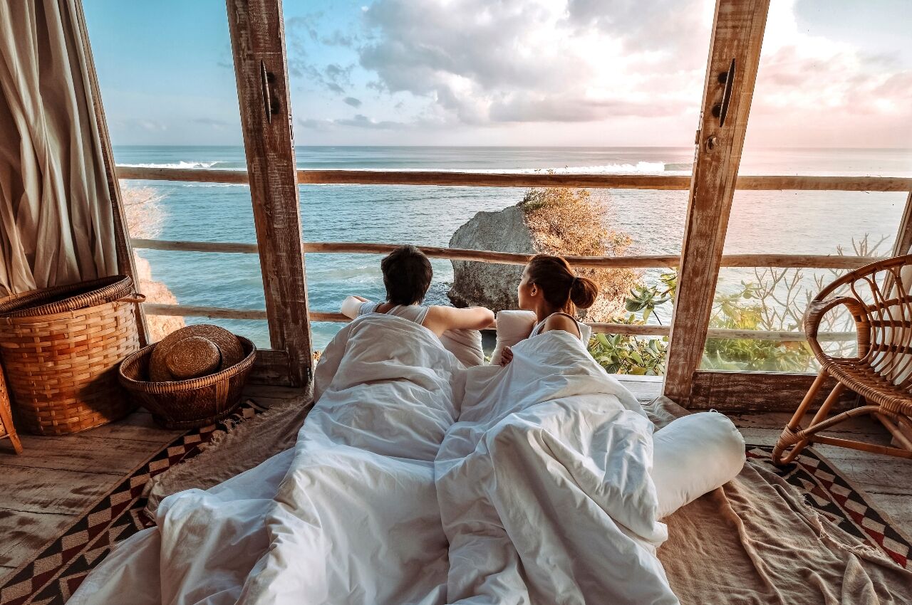 Couple in bed looking out of window with view over the coast in Bali 