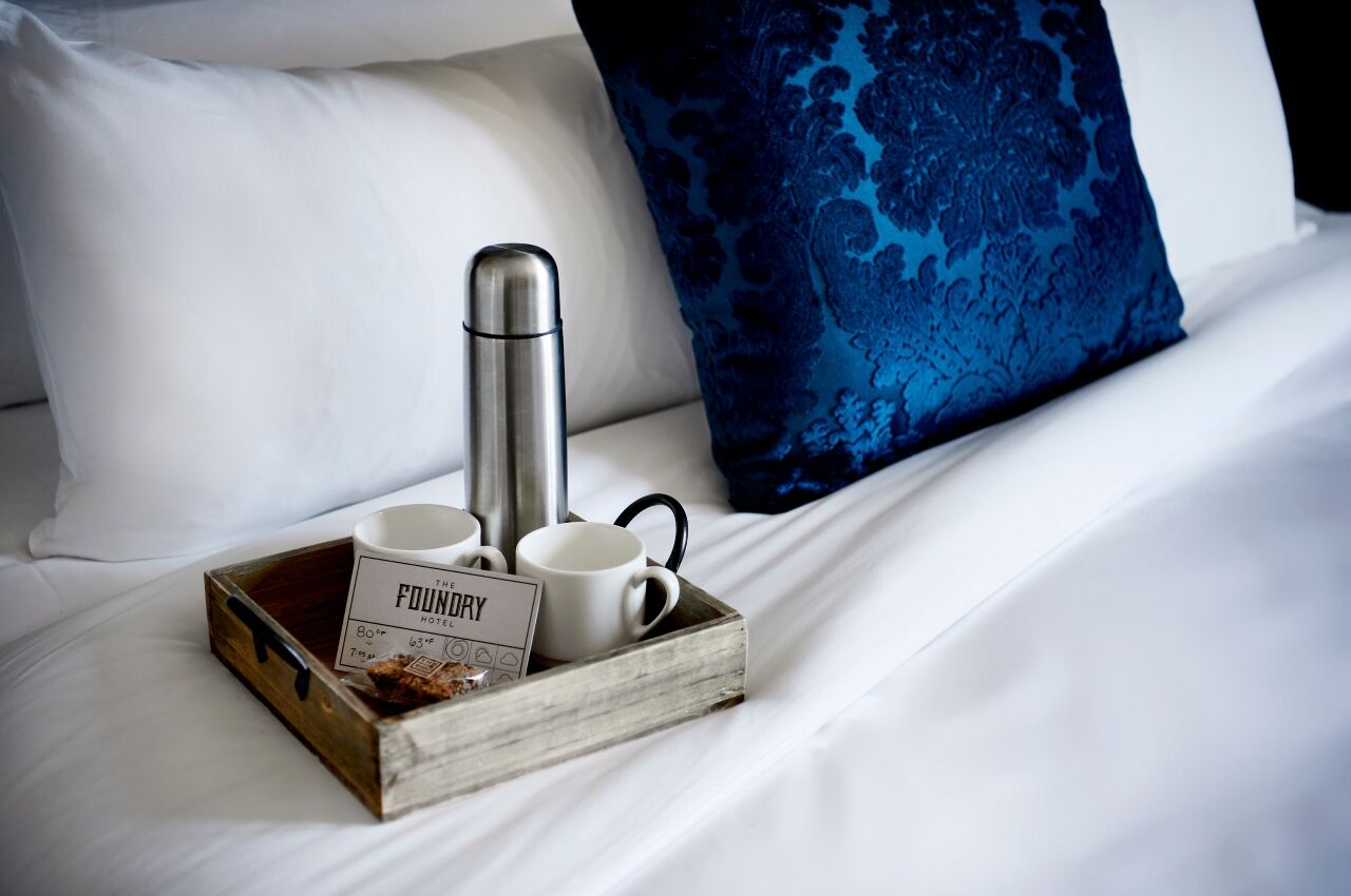 Luxury hotel amenities local tea in flask with two mugs on bed at The Foundry Hotel