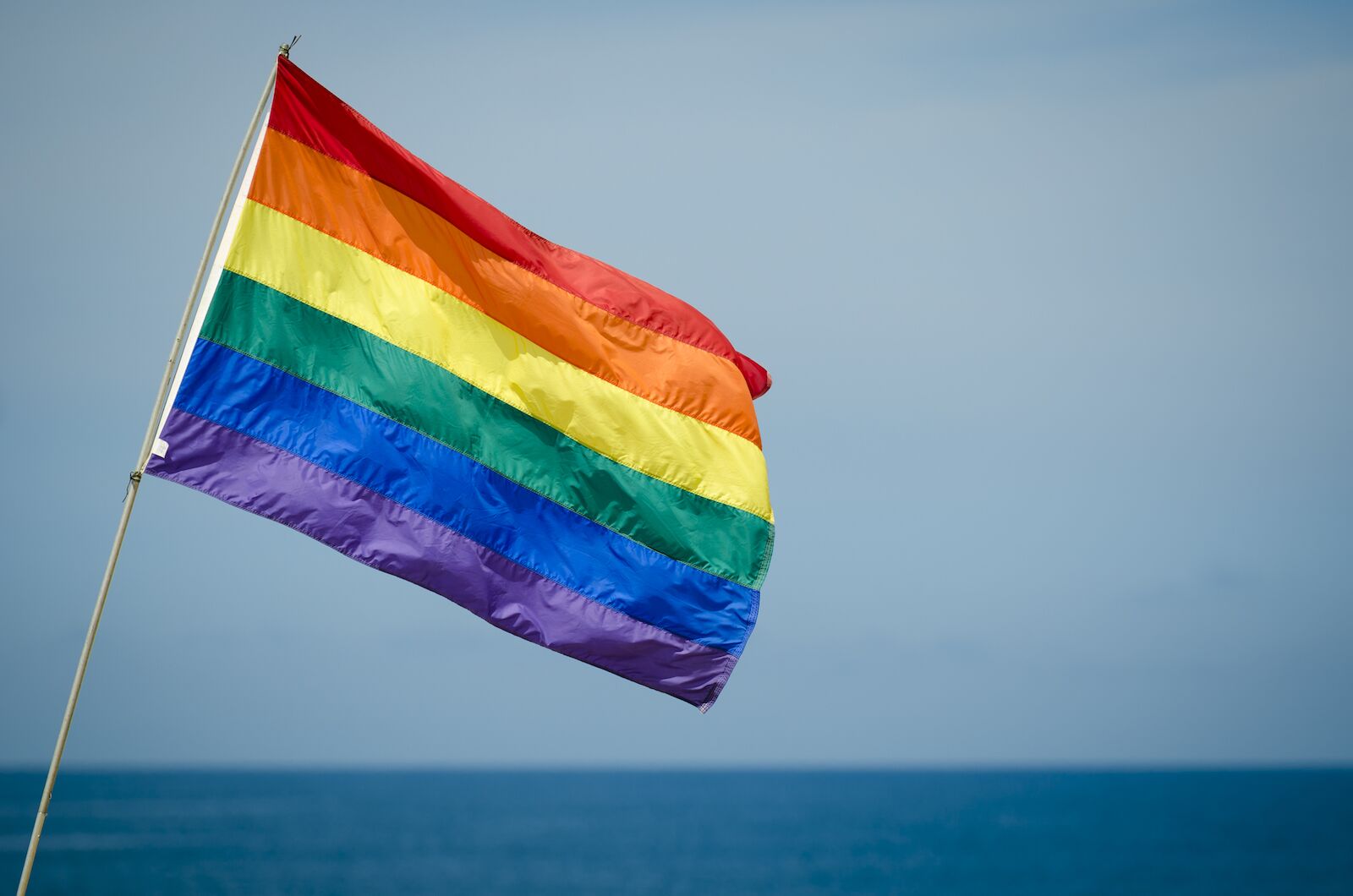 Gay pride rainbow flag flying outdoors in bright summer sun above the ocean horizon in Fire Island, New York
