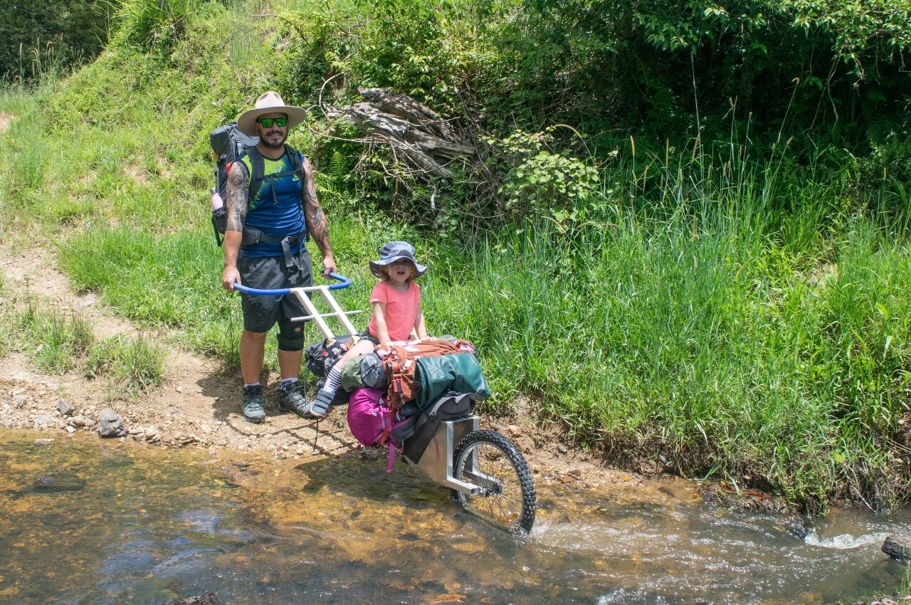 DIY carry buggie being pushed over river with kid on hike with kids