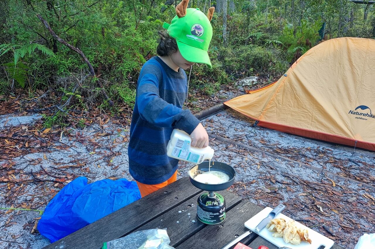 Young boy making pancakes at campsite during hike with kids in Australia