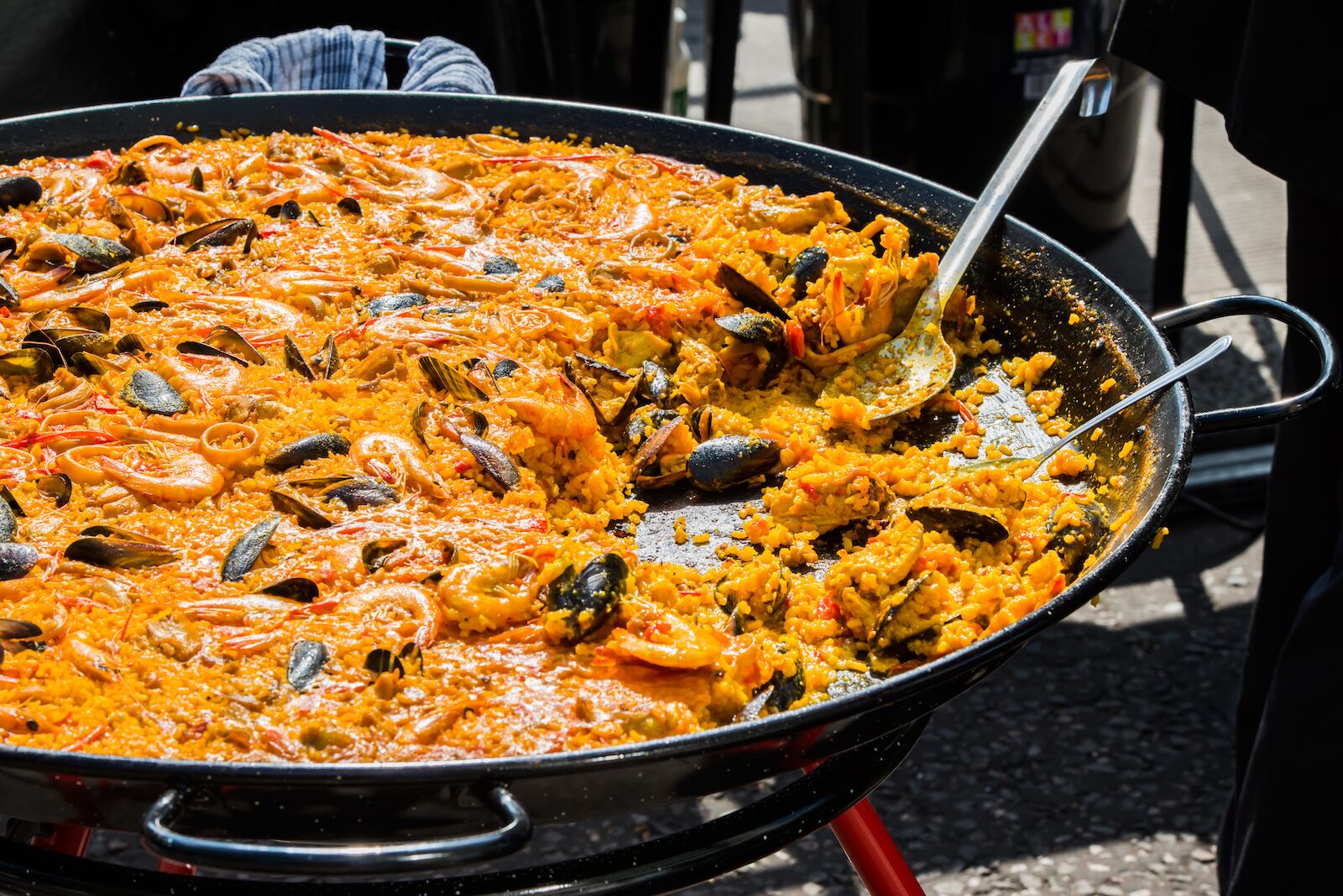 paella being cooked inside a large pan with a serving spoon-valencia foods