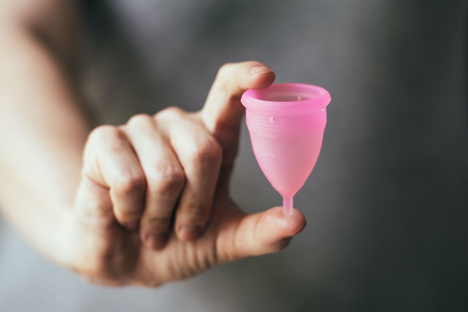 young woman holding a pink menstrual cup between her thumb and forefinger