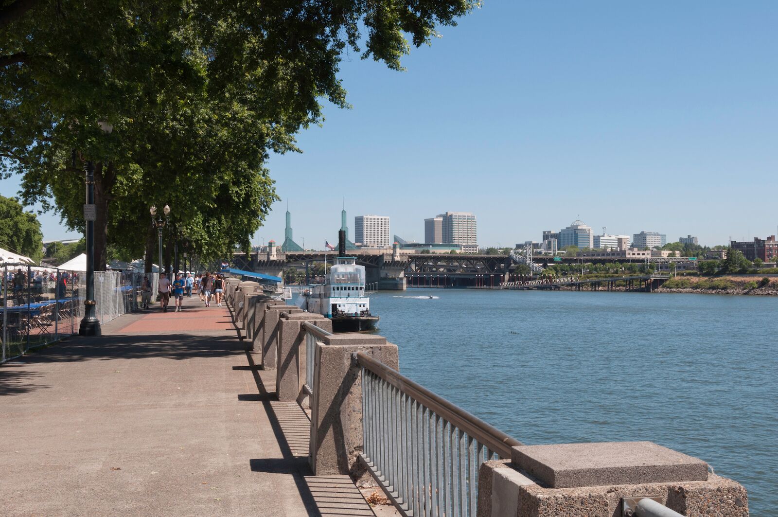 Portland, Oregon - July 24. 2010: Walkway along the Willamette River in Waterfront Park with the Portland Saturday Market stalls set up on the left side behind the fencing