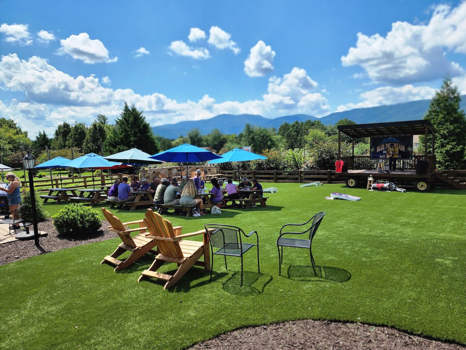 Lawn and stage at Blue Moutain Brewery with people sitting at tables under blue umbrellas on Nelson 151