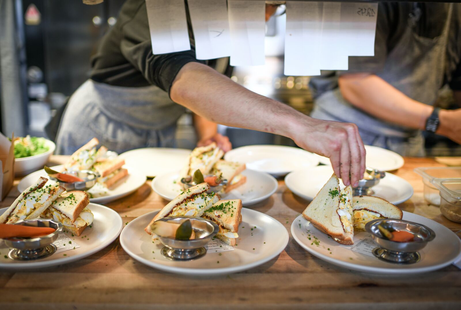 Several plates with sandwiches at Bell's restaurant waiting to be served with chefs in background - chepeast Michelin star restaurants in California