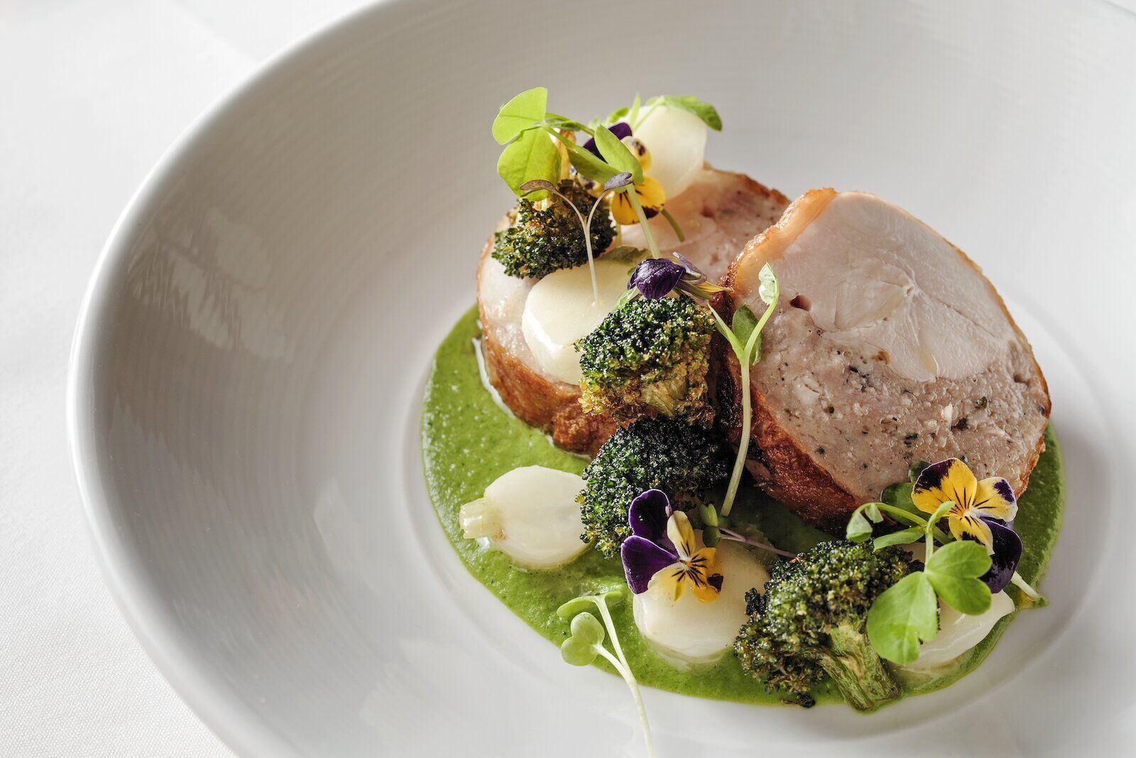 chicken ballotine in white bowl with green puree served at the village pub