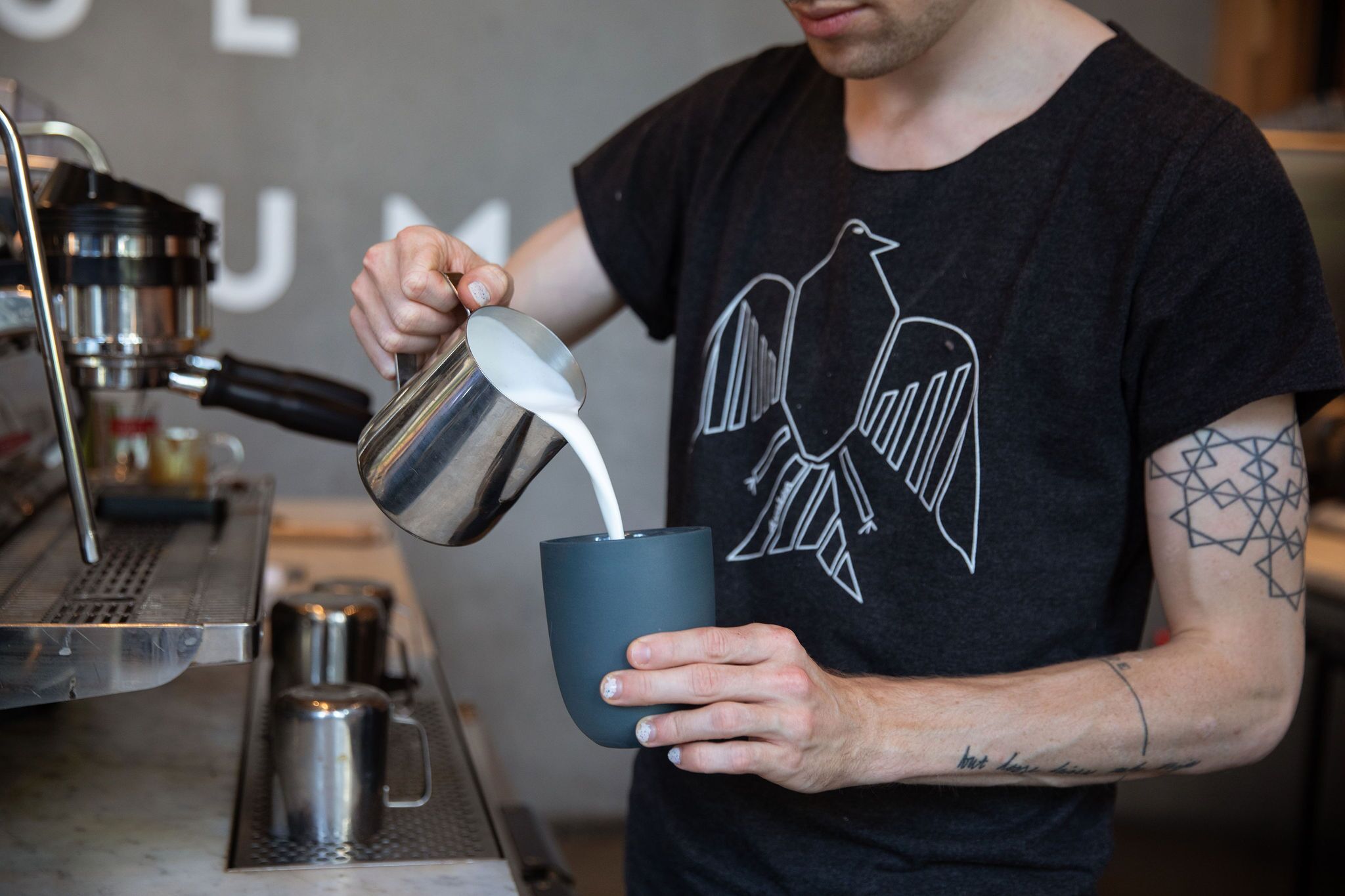 man pouring coffee standing next to espresso machine - seattle coffee shops