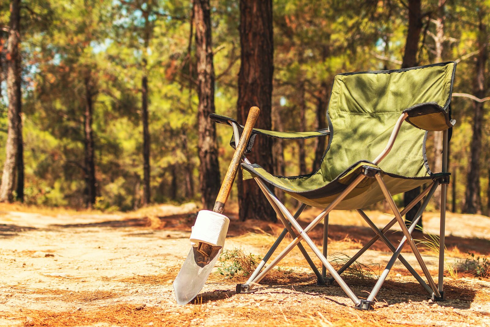 shovel and roll of toilet paper leaning up against a green camping chair in the woods - how to poop in the woods