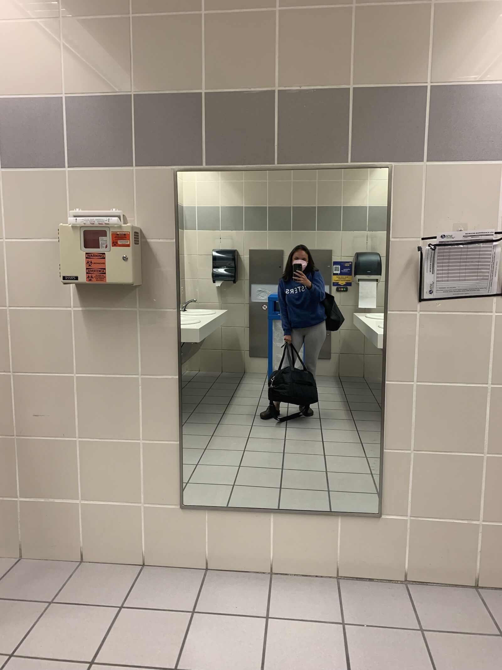 Woman in blue sweatshirt holding Lululemon duffle bag in airport bathroom